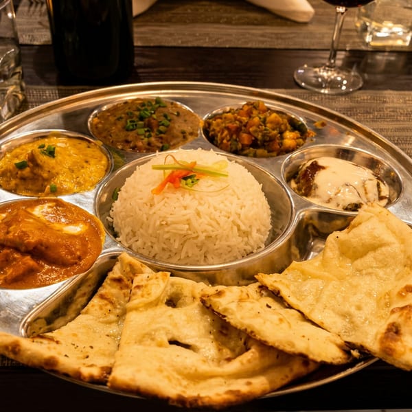 A metal thali platter with various Indian dishes, including rice, curries, and naan bread.