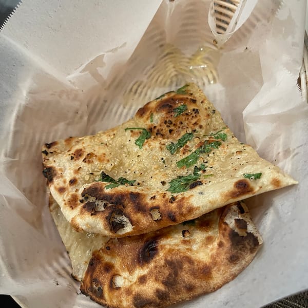 Golden brown naan bread, garnished with green herbs, served in a white paper-lined basket.