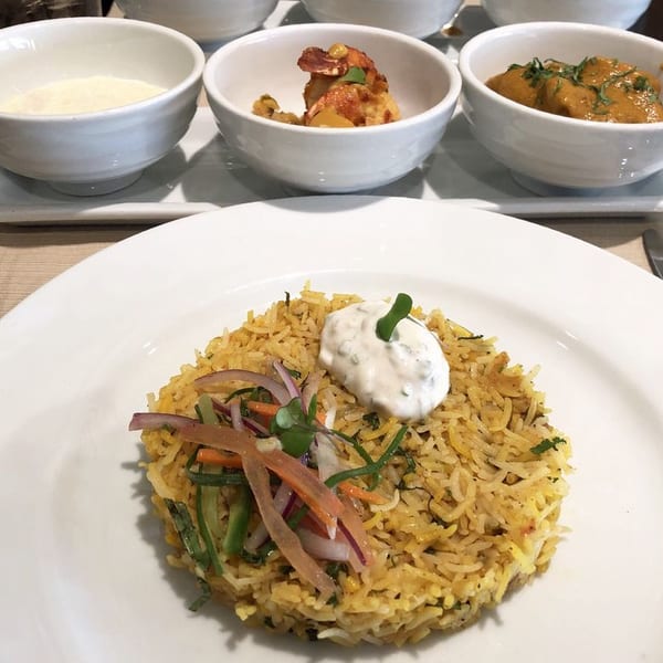 Indian biryani with raita and side dishes of curry, shrimp, and a white sauce.
