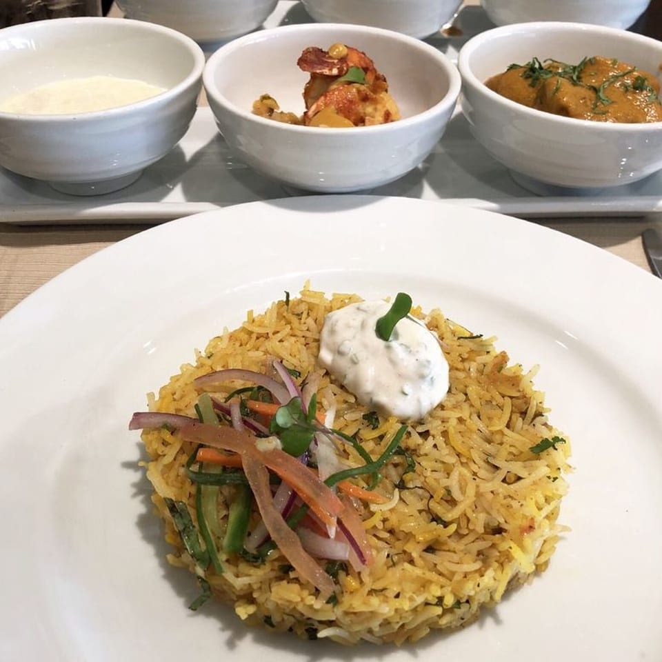 Indian biryani with raita and side dishes of curry, shrimp, and a white sauce.
