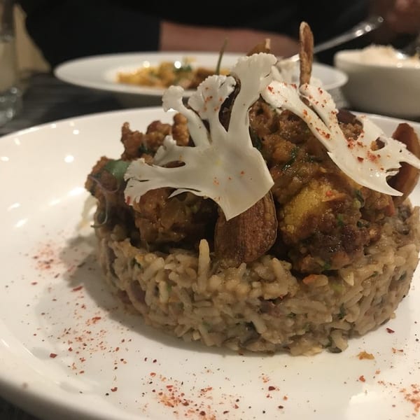A gourmet dish of rice topped with curried vegetables and cauliflower crisps on a white plate.