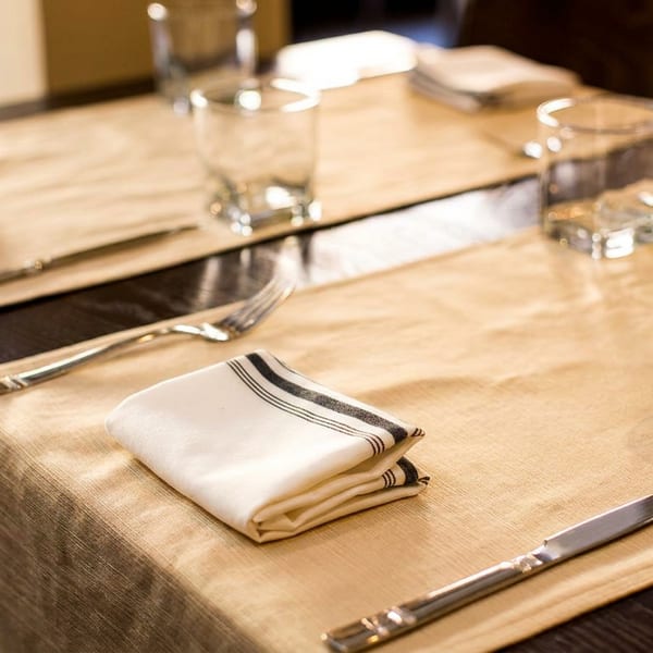 Two elegantly set dining tables with beige runners, white napkins, and glassware.
