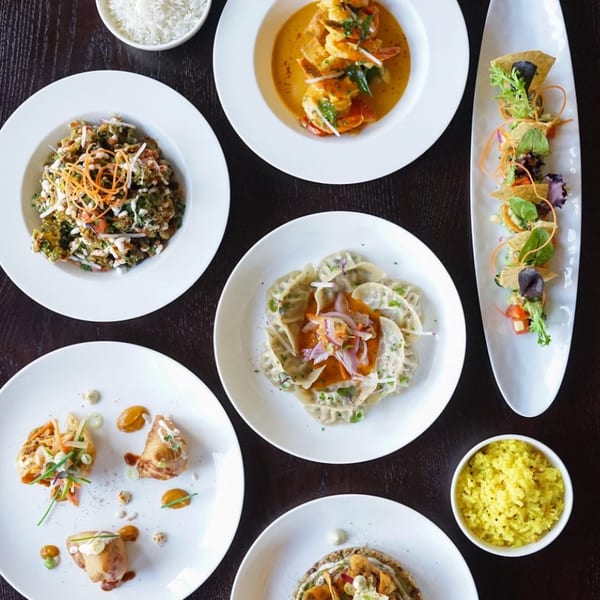 An overhead view of various beautifully plated dishes, including shrimp, dumplings, and rice, on a dark table.