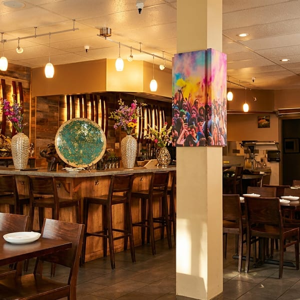 Restaurant interior with a bar, wooden tables, chairs, and colorful decor under warm lighting.