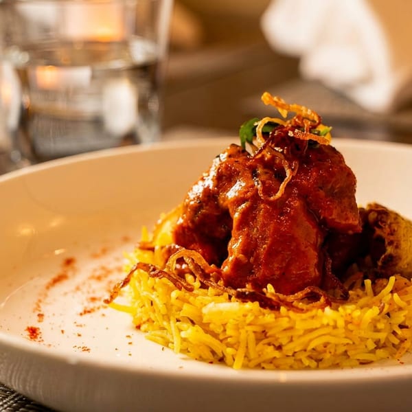 A vibrant dish of red curry chicken and yellow rice, garnished with crispy fried onions.